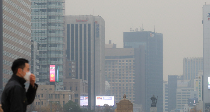 A person wearing a mask walking in a city filled with smog.